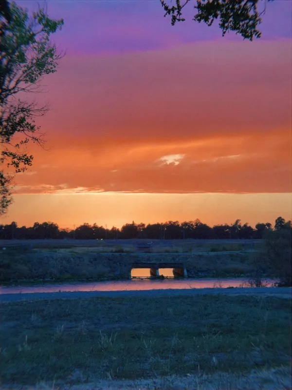 Orange sky over a creek and a small bridge, violet clouds above