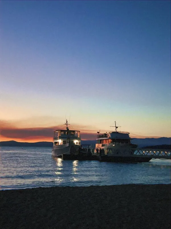 Two lit-up boats at a pier on a lake after sunset