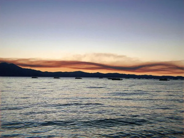 A twisting orange band of cloud over a mountain lake at dusk